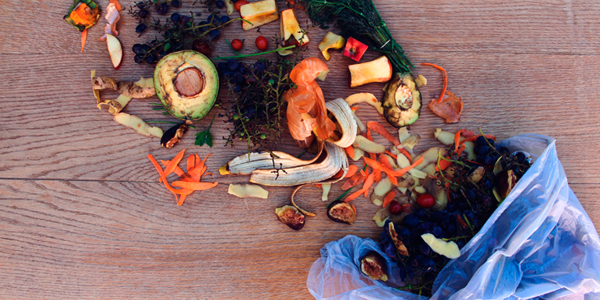 Plastic bag on the floor, with compostable waste flowing out, such avocados, a banana peel, and other peelings