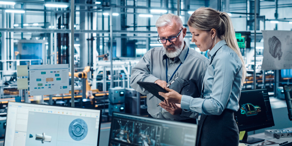 Automotive manufacturer setting. Two employees are viewing a tablet. CAD drawings can be seen within the office.