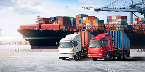 Two trucks in front of a cargo ship with freight